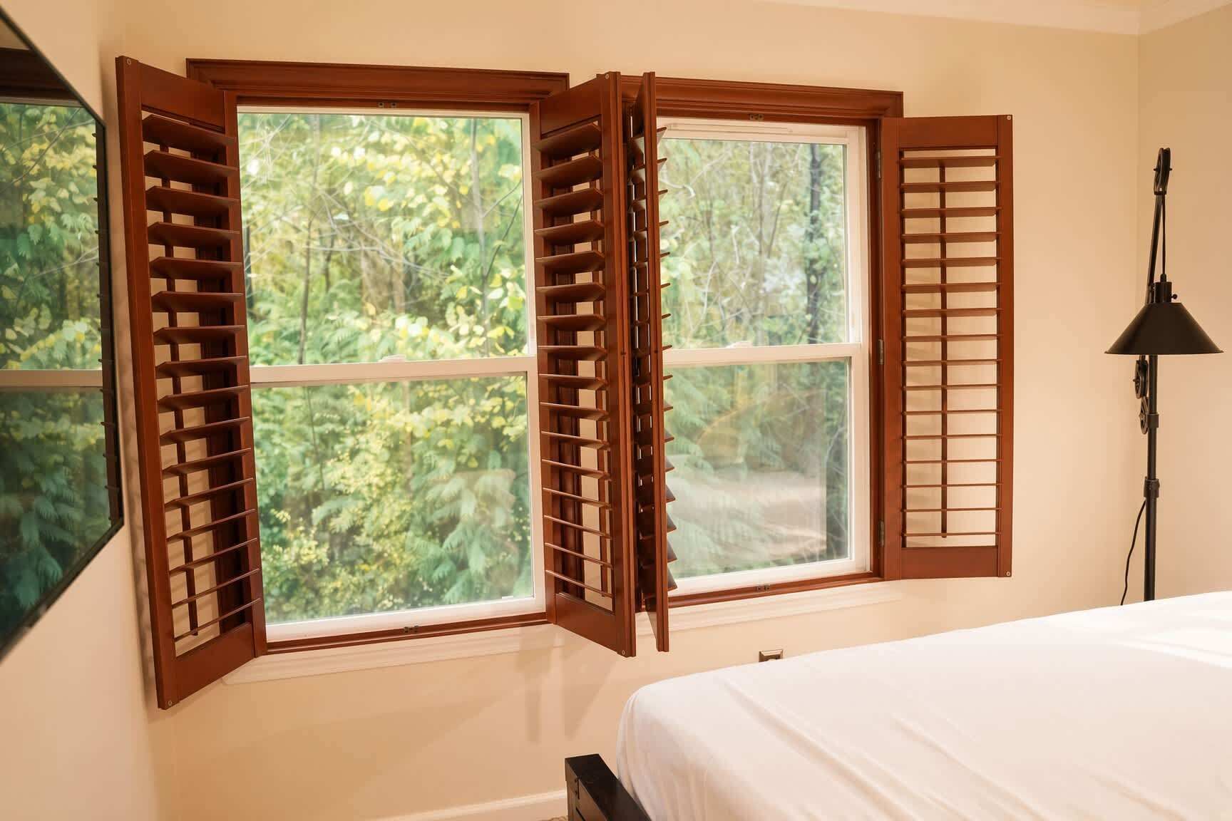 A bedroom with a bed, a window with wooden shutters, and a lamp.