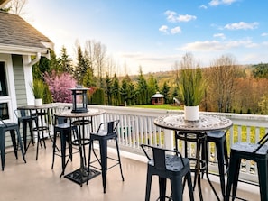 Une terrasse couverte avec des tables et des chaises rondes, une lanterne et une vue sur un paysage boisé.