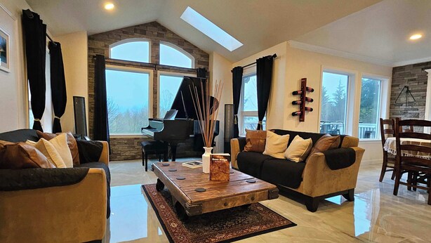 Un salón espacioso con un piano de cola, dos sofás, una mesa de centro y amplias ventanas que ofrecen vistas al exterior.