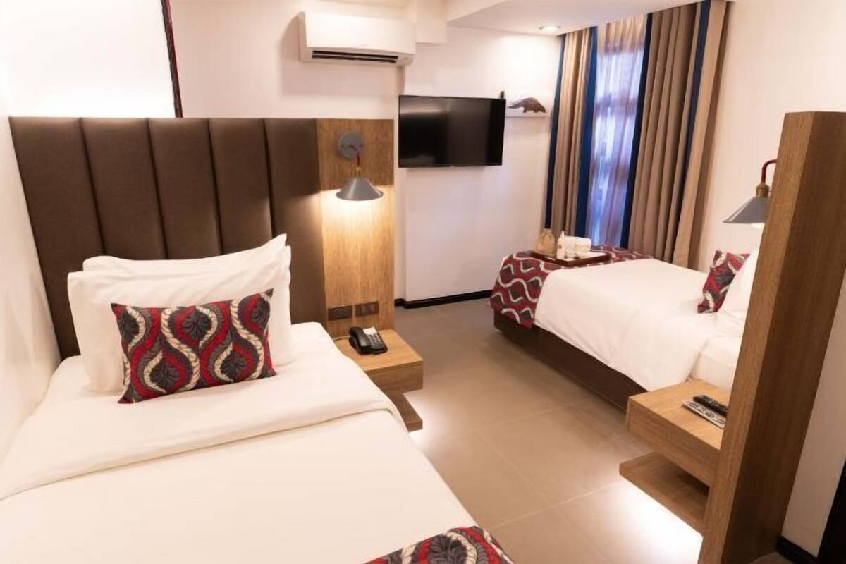 A hotel room with a large bed, a smaller bed, a TV, and a desk with a lamp.