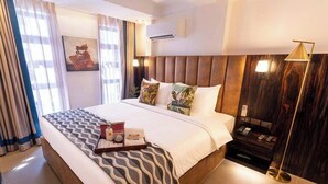 Quarto de hotel com uma cama grande, mesas de cabeceira, um criado-mudo, uma luminária e ar condicionado fixado na parede.