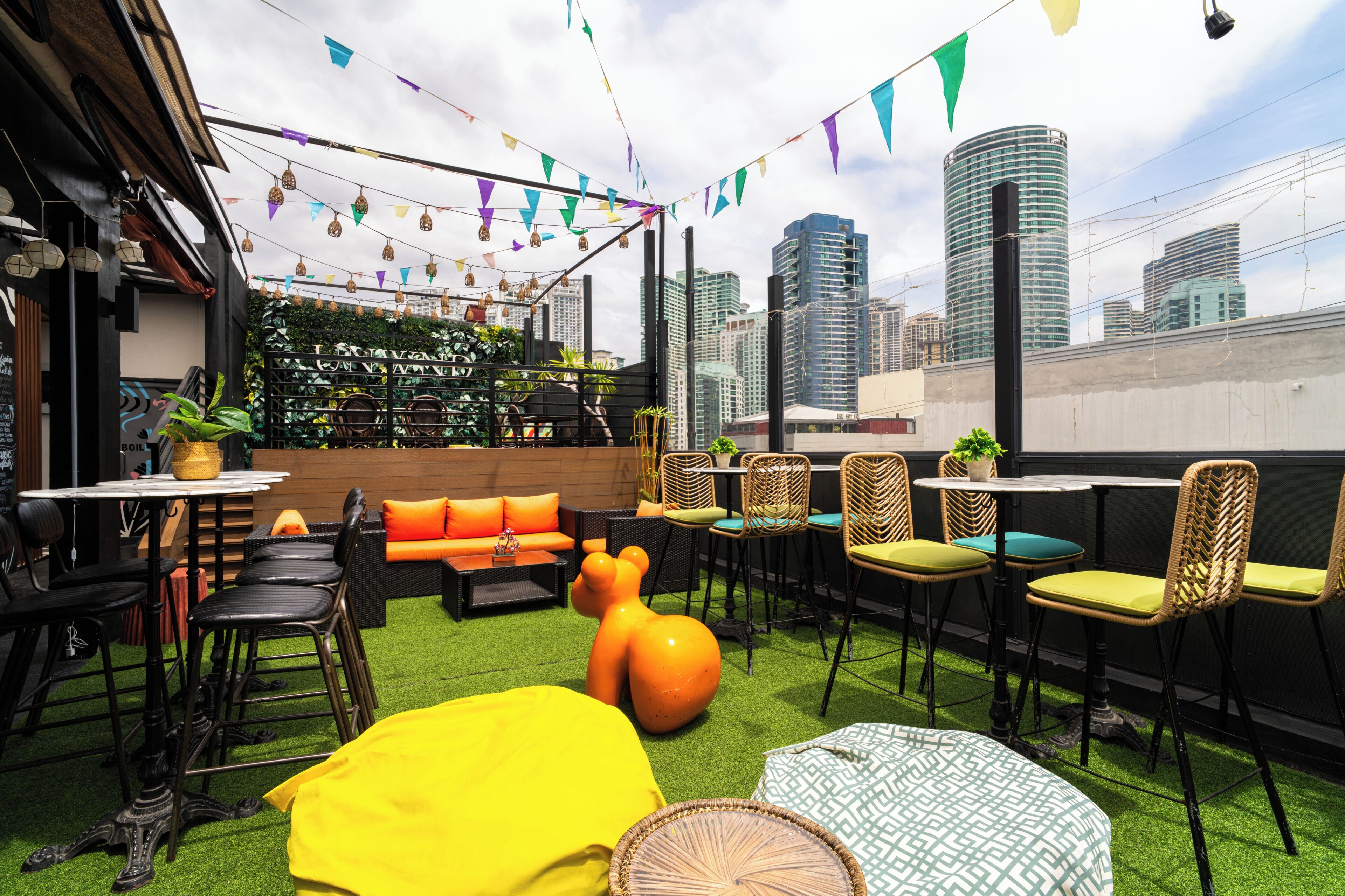 Un espace extérieur aménagé avec des tables, des chaises et un canapé, entouré de verdure et offrant une vue sur la ville.