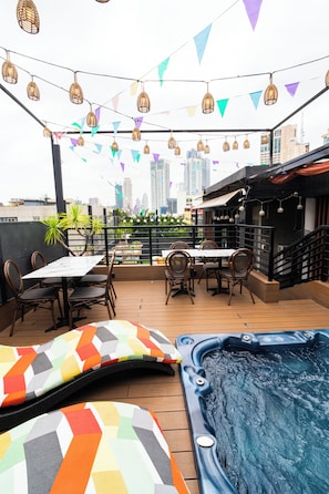 An outdoor patio with a hot tub, tables, chairs, and string lights.