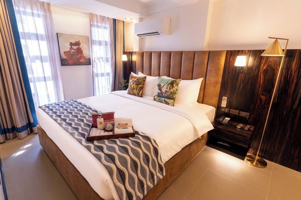 A hotel room with a large bed, a bedside table with a lamp, and a wall-mounted air conditioner.