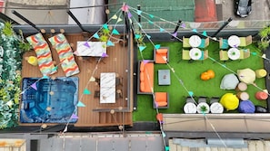 A rooftop patio with a hot tub, seating area, and a small lawn with tables and chairs.