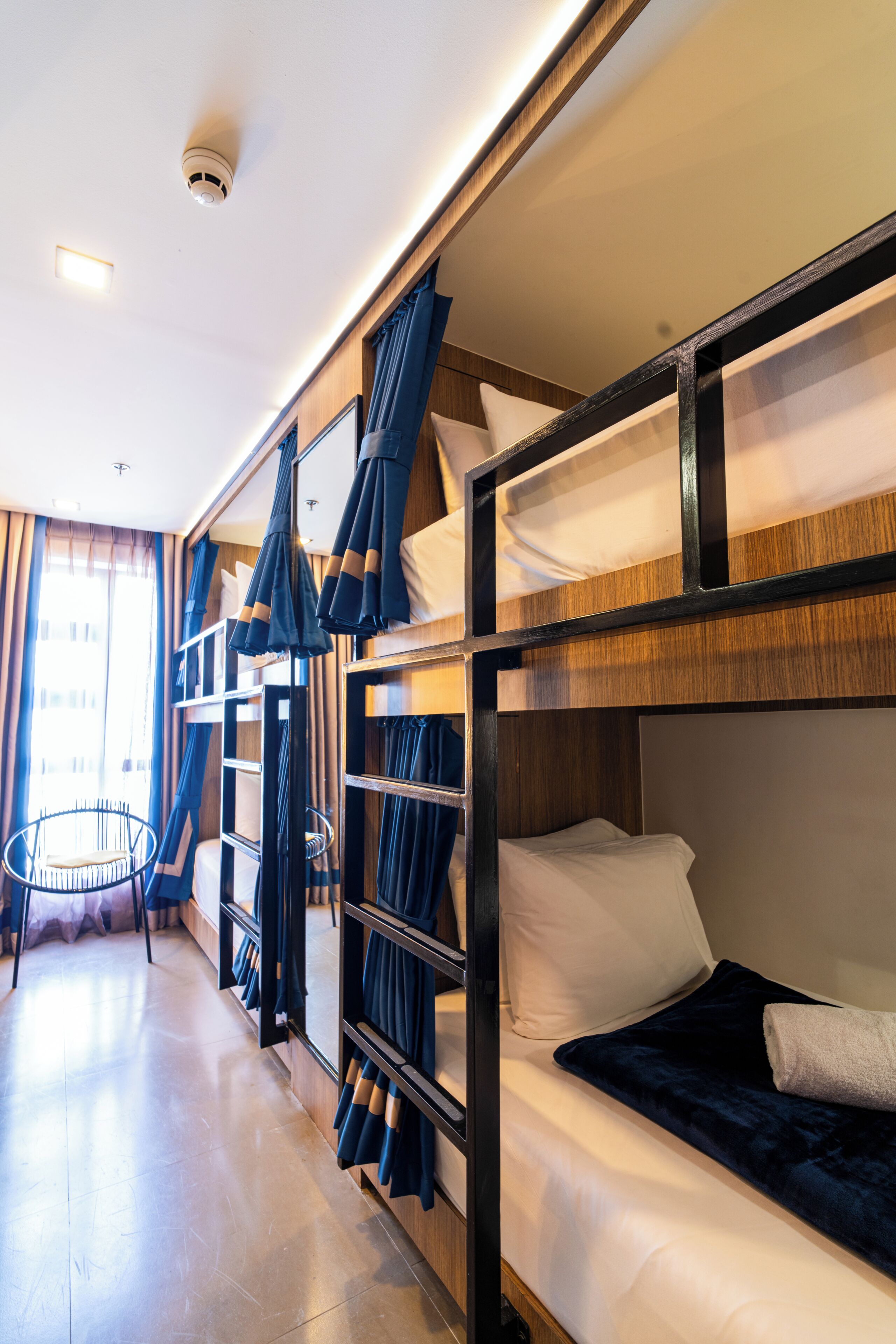 Dormitorio con literas, una silla, cortinas y una lámpara en el techo.