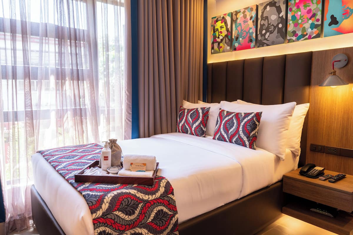 A hotel room with a bed, a bedside table with a lamp, a phone, and a tray with toiletries.