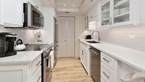 A modern kitchen with white cabinetry, stainless steel appliances, and a wooden floor. - Completely renovated condominium (St Simons)