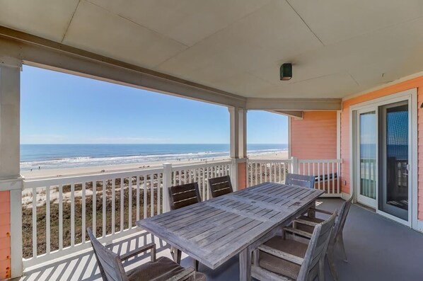 Ein überdachter Außenbereich mit Holztisch und Stühlen mit Blick auf einen Strand.