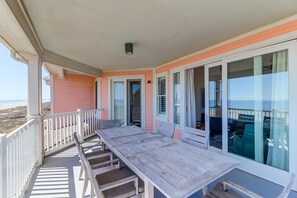 Ein überdachter Balkon mit Holztisch und -stühlen, großen Fenstern und Blick auf den Strand.