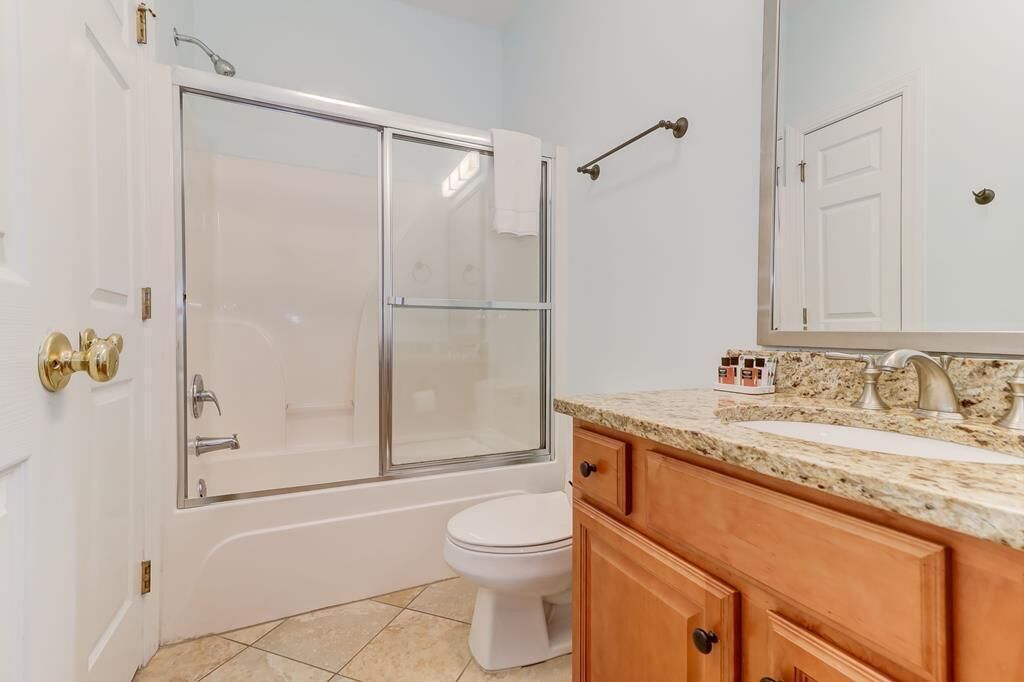 A bathroom with a glass-enclosed shower, a white toilet, wooden cabinets, and a marble countertop.