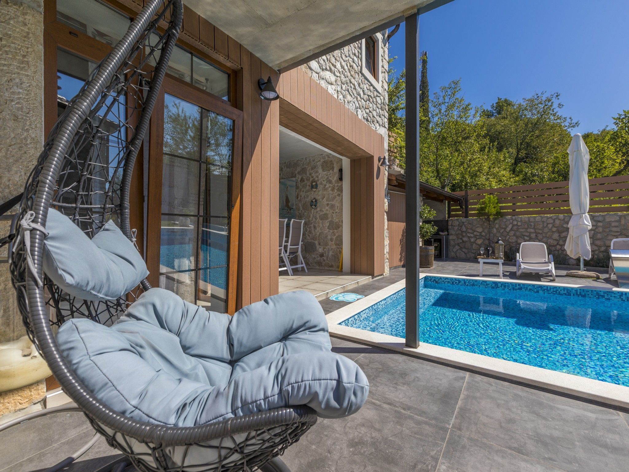 A modern outdoor pool area with a hanging chair, stone walls, and a clear view of the pool.