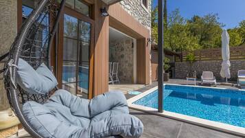 A modern outdoor pool area with a hanging chair, stone walls, and a clear view of the pool.