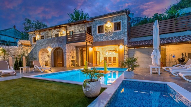 Une maison en pierre à deux étages, dotée d’une piscine, d’un espace extérieur aménagé et d’une terrasse bien éclairée.