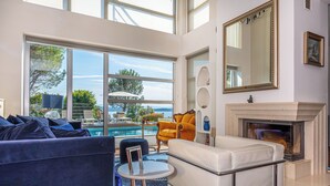 A modern living room with a fireplace, large windows overlooking a pool, and a view of the outdoors. - Villa Hana (Dramalj)