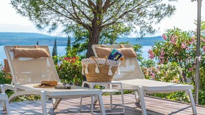 Two white lounge chairs with towels and a woven basket with a hat and sunglasses on a wooden deck with a view of a lake and trees. - Villa Hana (Dramalj)