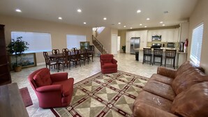 A spacious living area with a dining table, red armchairs, a patterned rug, and a kitchen in the background. - Hope House, resort style with mountain view (Perris)