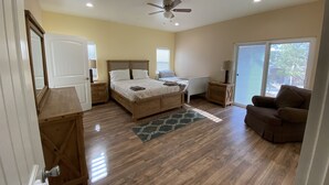 A bedroom with a wooden bed, a ceiling fan, a nightstand, a dresser, a chair, and a sliding glass door leading to a balcony. - Hope House, resort style with mountain view (Perris)