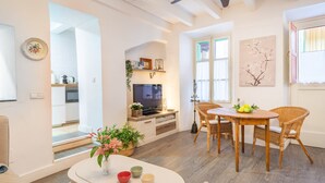 Un salon moderne comprenant un coin repas, un téléviseur et une cuisine visible à travers une porte ouverte.