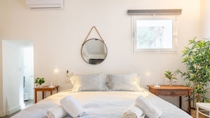 Un lit bien fait, avec des oreillers, une table de chevet avec une lampe, un miroir au mur et une fenêtre donnant sur un beau paysage.