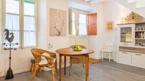Une pièce avec une table en bois, des chaises en osier, un meuble blanc aux portes vitrées et une œuvre d’art accrochée au mur.