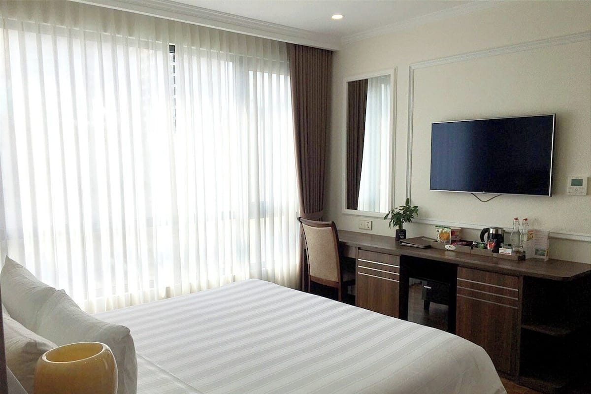 A hotel room with a bed, a desk, a chair, a TV, and a window with curtains.