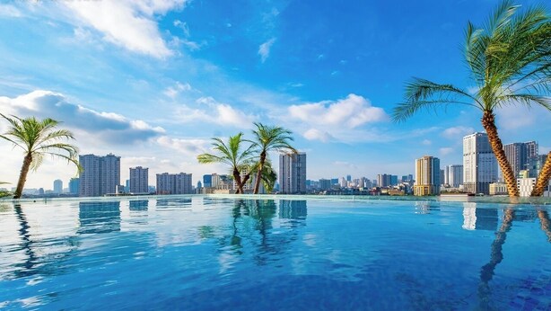 Una piscina con palmeras y un horizonte urbano al fondo.
