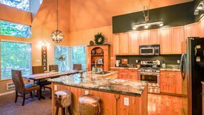 Une cuisine avec des meubles de rangement en bois, un plan de travail en granit et un îlot central doté de tabourets.