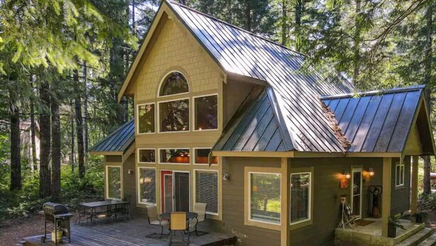 Une cabane à deux étages avec une terrasse, entourée de forêt.