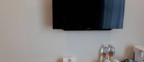 A hotel room with a flat-screen TV mounted on the wall, a non-smoking sign, bottled water, and a hairdryer on the wooden table.