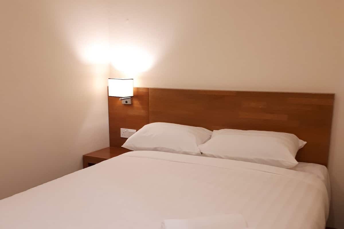 A neatly made bed with white linens and pillows, a wooden headboard, and a bedside table with a lamp.