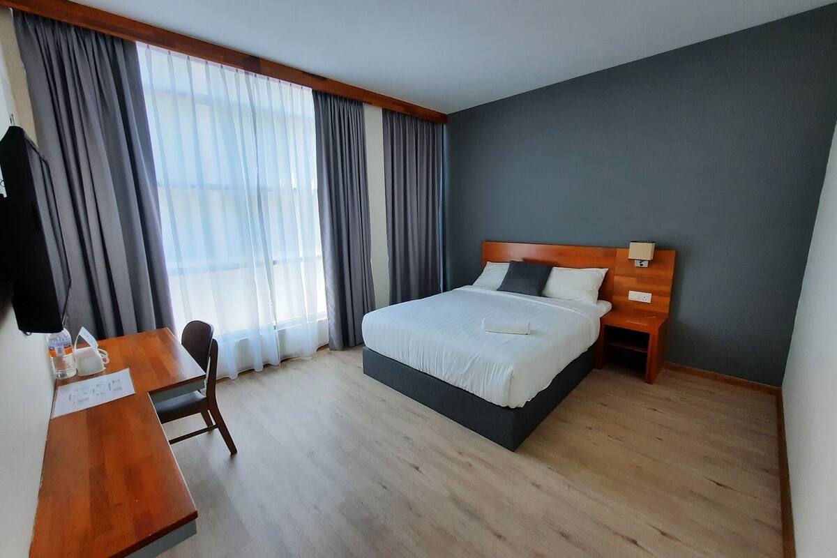 A hotel room with a large bed, wooden headboard, a desk with a chair, and a nightstand.
