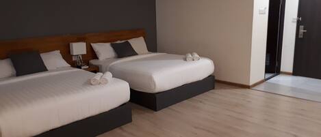 A hotel room with two beds, a wooden headboard, a nightstand, and a door.