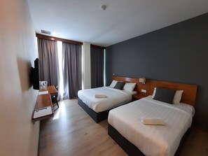 Habitación de hotel con dos camas, un escritorio con teléfono y una ventana con cortinas.