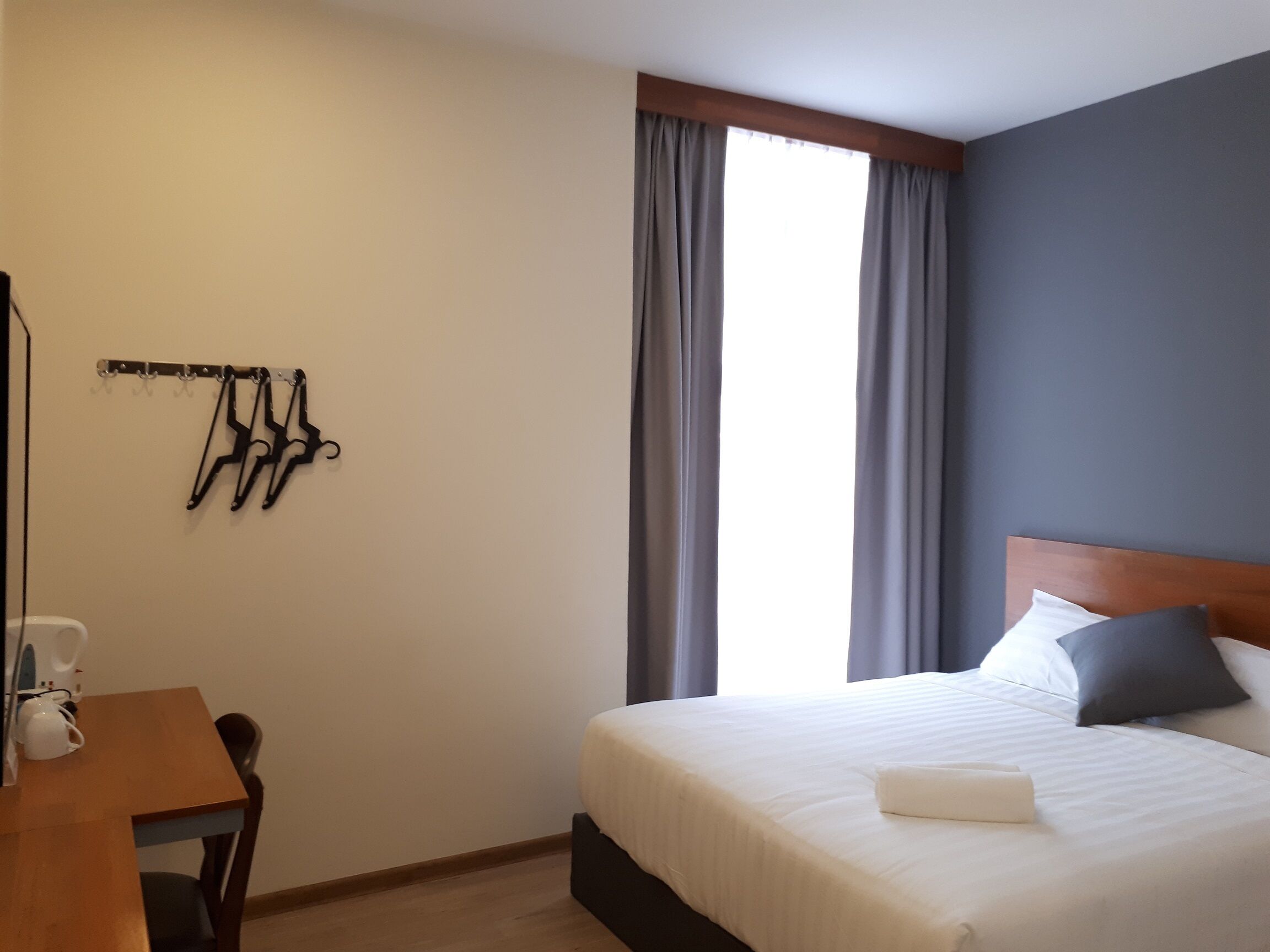 A hotel room with a bed, a desk, and a window with curtains.