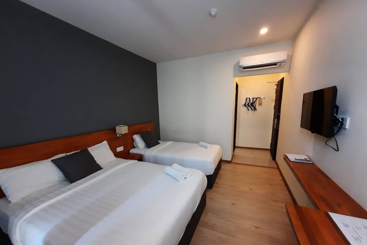 A hotel room with two beds, a wooden headboard, a flat-screen TV, and an air conditioning unit.
