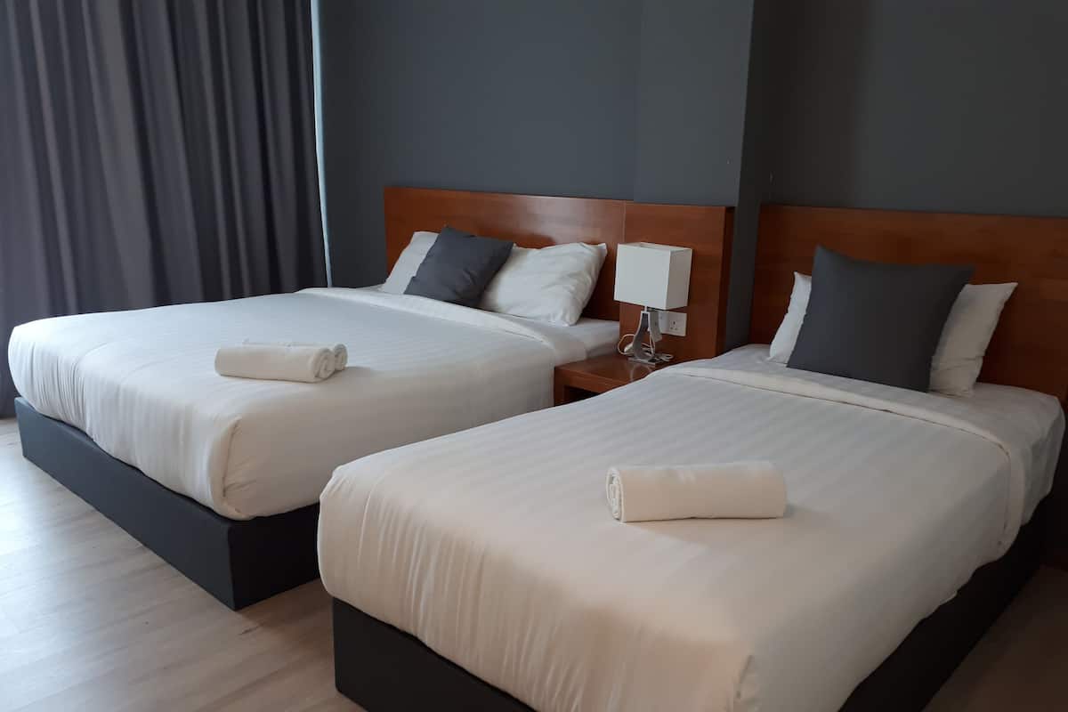 Two adjacent beds with white linens, a wooden headboard, and a bedside table with a lamp.