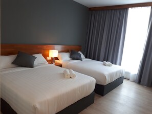 A hotel room with two beds, a nightstand with a lamp, and a large window with curtains.