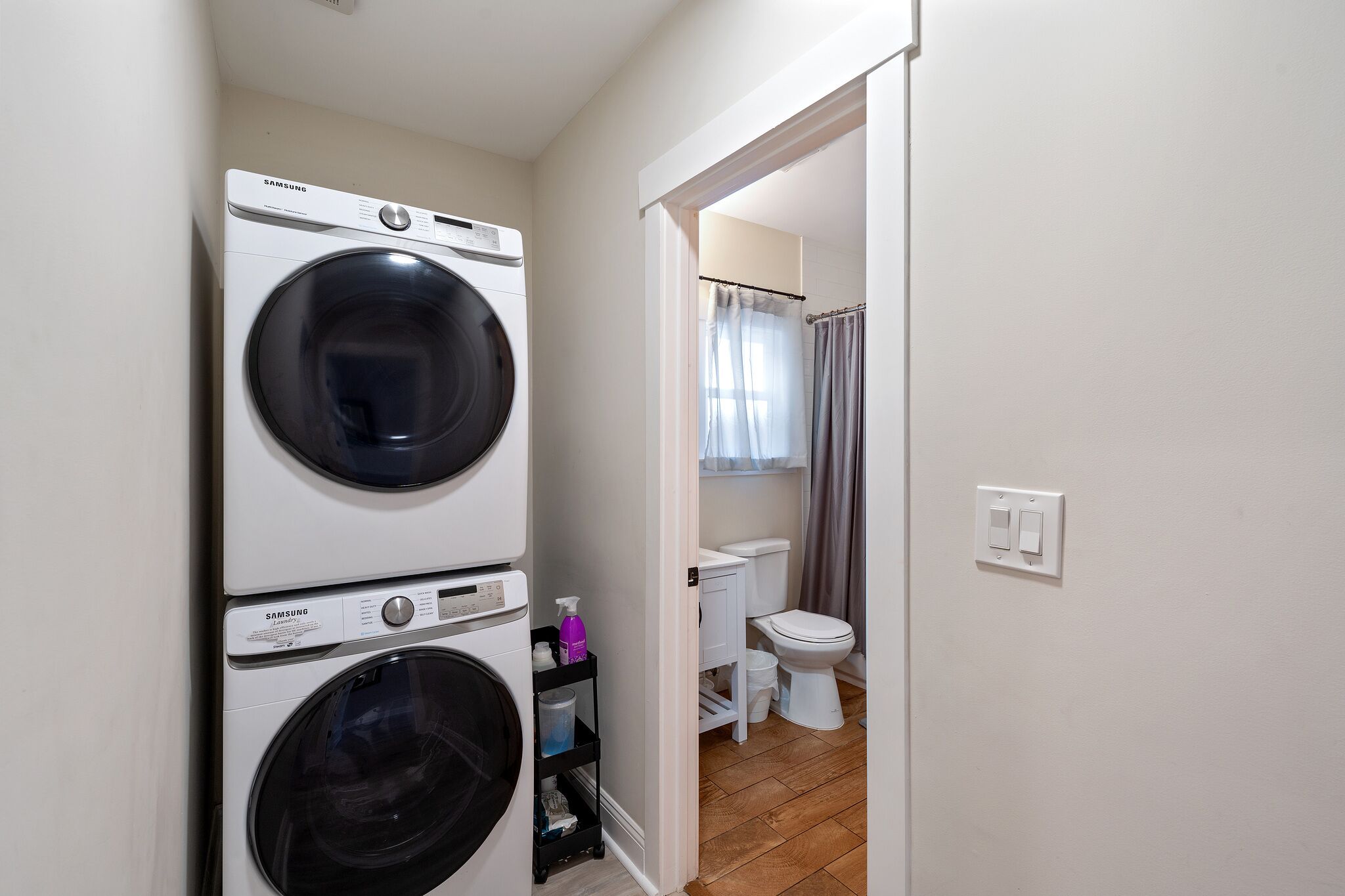 A laundry area with two stacked washing machines, a toilet, and a shower curtain.