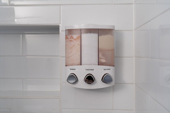 A wall-mounted dispenser with three compartments labeled for shampoo, conditioner, and body wash.