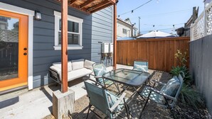 A patio with a glass table and chairs, a wooden deck, and a fenced backyard.