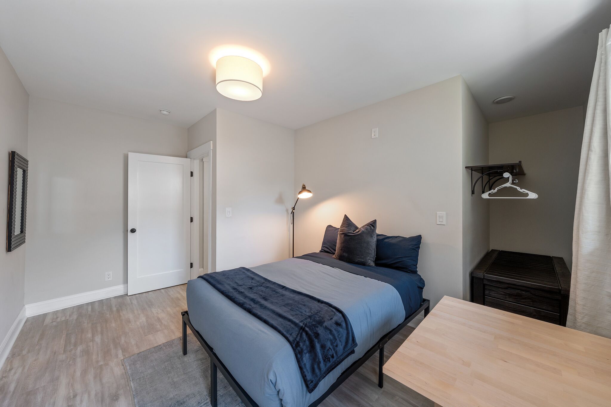 A bedroom with a bed, bedside table, lamp, and a coat hanger.