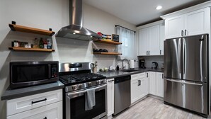 A modern kitchen with stainless steel appliances, white cabinetry, and wooden shelves.