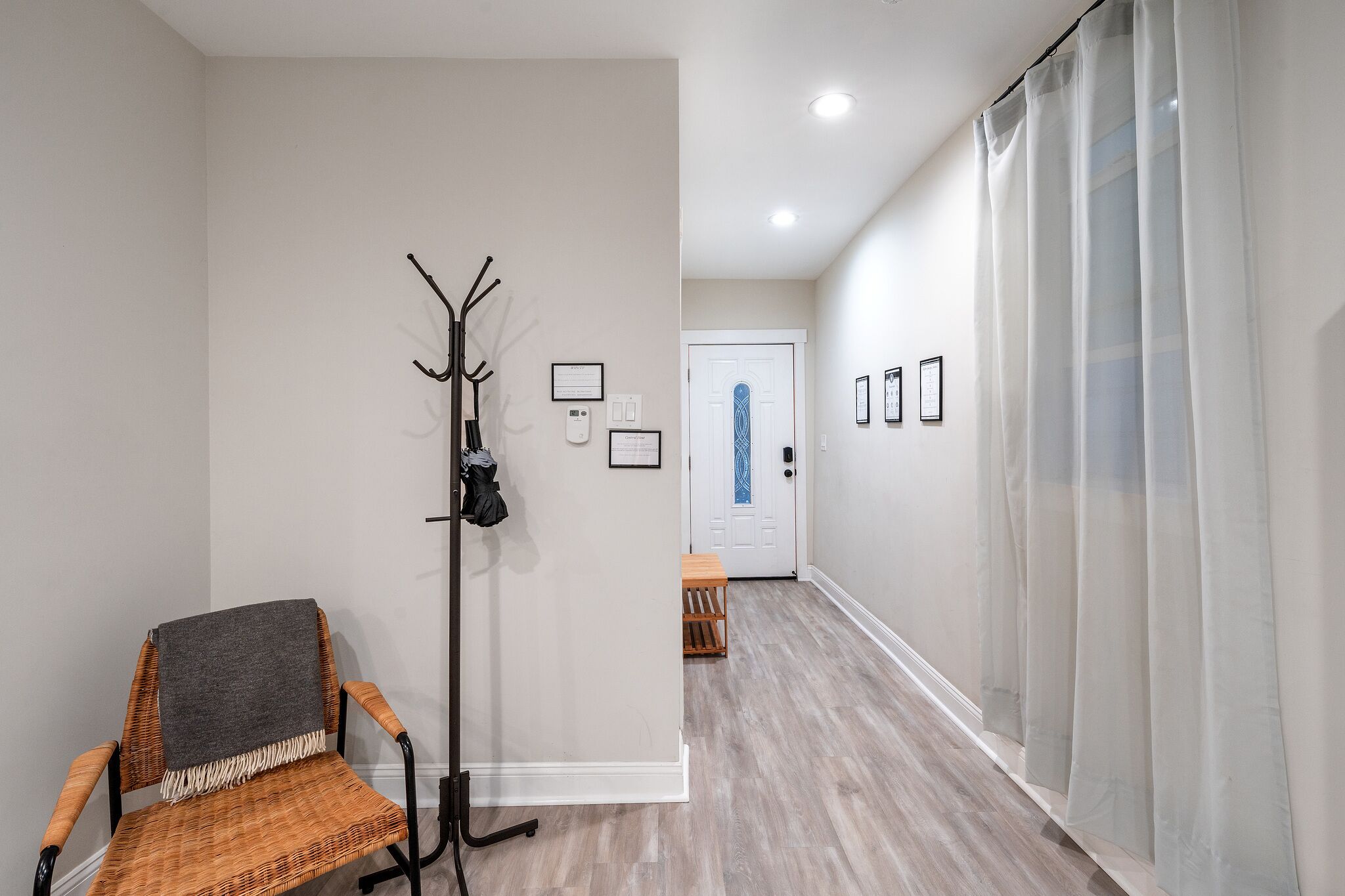 A hallway with a coat rack, a chair with a blanket, and a door at the end.