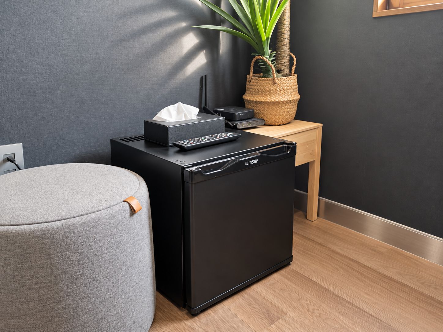 A compact black appliance, possibly a dishwasher, on a wooden table with a tissue box and remote control.