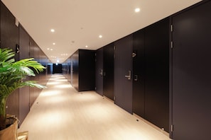 A corridor with wooden flooring, dark-colored lockers, and a potted plant on the left. - Brosis Hotel (Busan)
