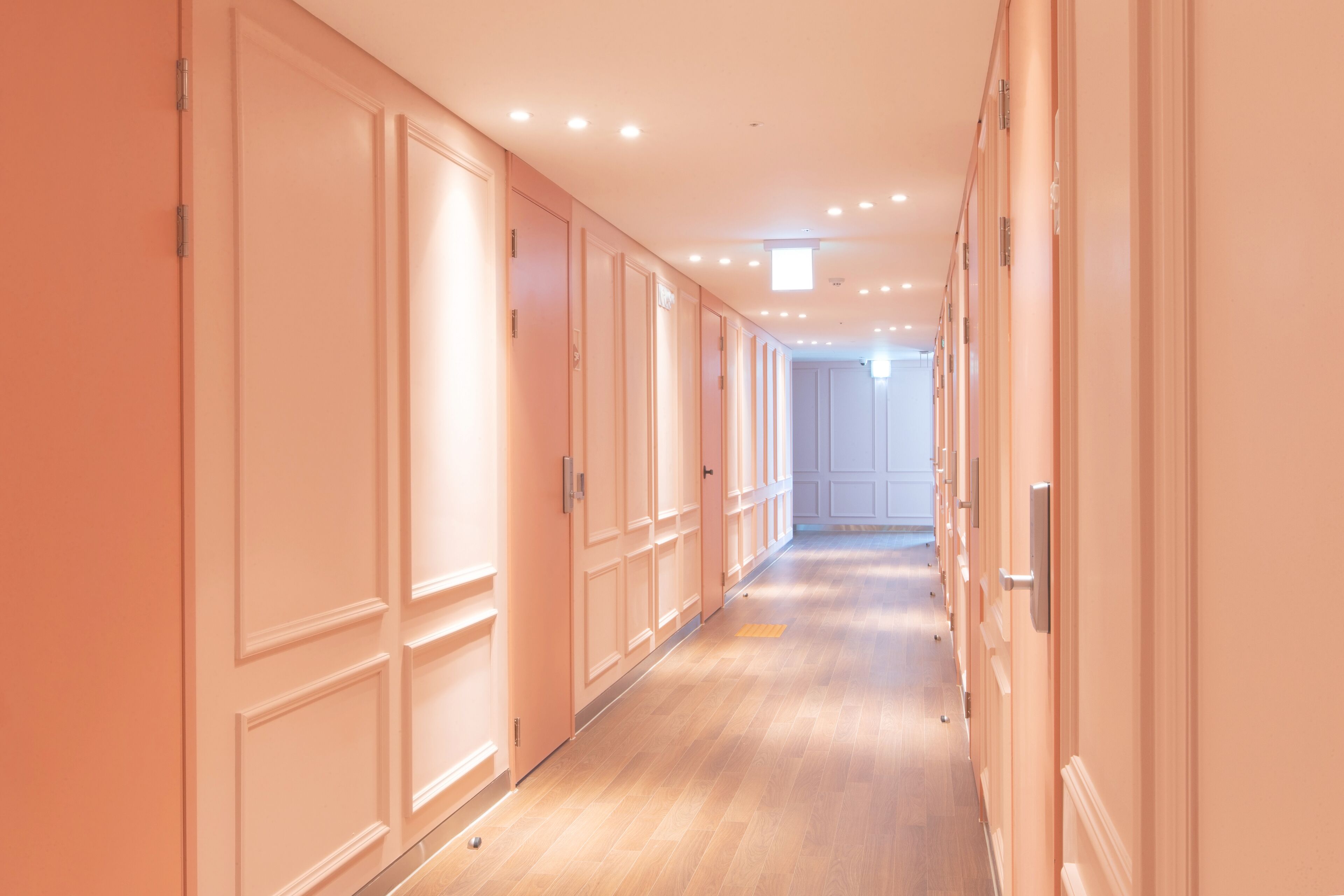 A long hallway with doors on both sides, wooden flooring, and recessed ceiling lights.