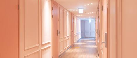 Un largo pasillo con puertas a ambos lados, suelo de madera y luces empotradas en el techo.
