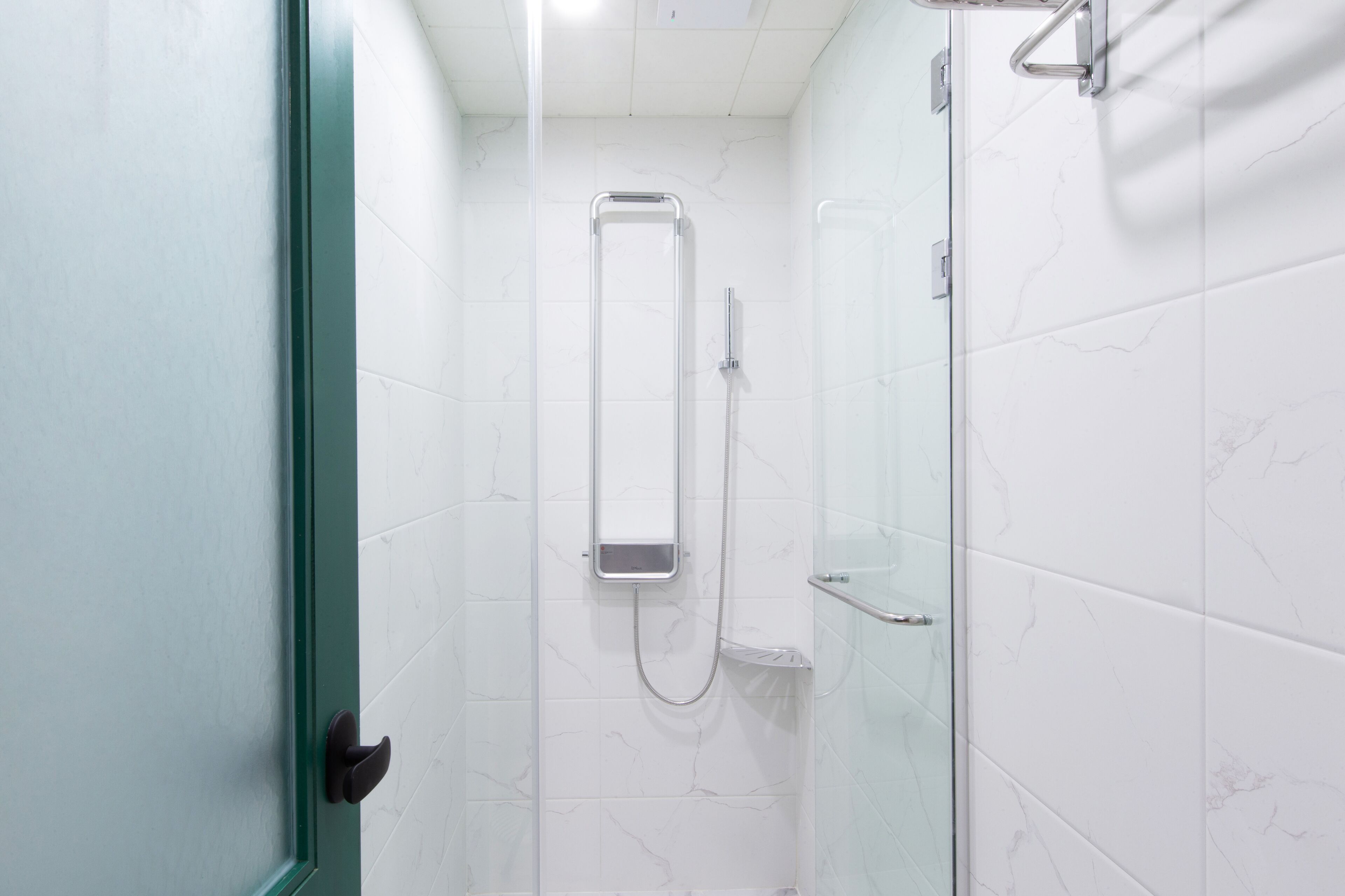 A bathroom with white marble tiles, a glass shower enclosure, and a metal grab bar.