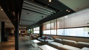 Un lobby moderno con un amplio espacio de descanso, una recepción y vistas de la ciudad a través de grandes ventanales.